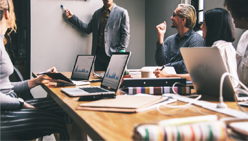 Reunião de negócios com profissionais reunidos ao redor de uma mesa, usando laptops e participando de uma apresentação em estilo corporativo. Imagem usada para ilustrar o artigo que aborda os conceitos e como fazer um Programa nos Lucros e Resultados (PLR) efetivo.