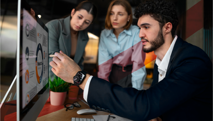 Homem apresentando dados em um computador por meio de um software de execução estratégica. Ele está reunido com duas mulheres em ambiente de escritório, discutindo estratégias de negócios ou análise de dados.