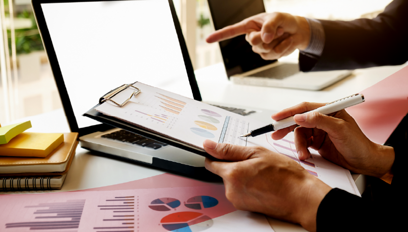 Dois profissionais analisando gráficos e relatórios de desempenho impressos sobre a mesa, representando a avaliação de resultados para programas de PPR e PPL.