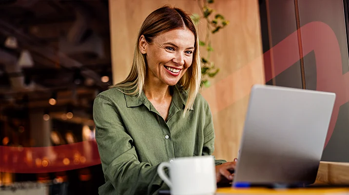Mulher sorridente trabalhando em laptop em ambiente de café moderno, ilustrando um artigo da Siteware sobre remuneração variável.