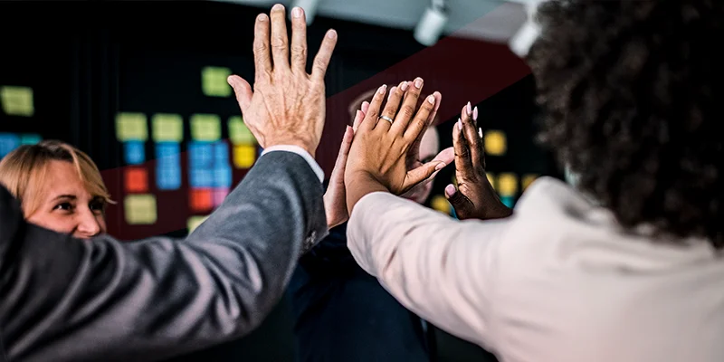 Equipe de negócios comemorando com high five coletivo em ambiente de escritório moderno, ilustrando um artigo da Siteware sobre excelência operacional​.