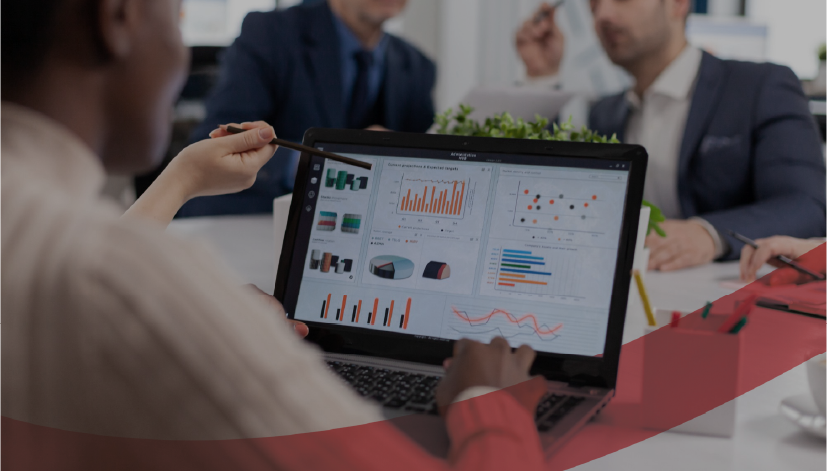 Profissional apresentando um dashboard executivo com múltiplos gráficos e indicadores em reunião de gestão, com líderes ao fundo analisando os resultados. O dashboard é visto por meio da funcionalidade de Relatórios e Gestão à Vista do Stratws.